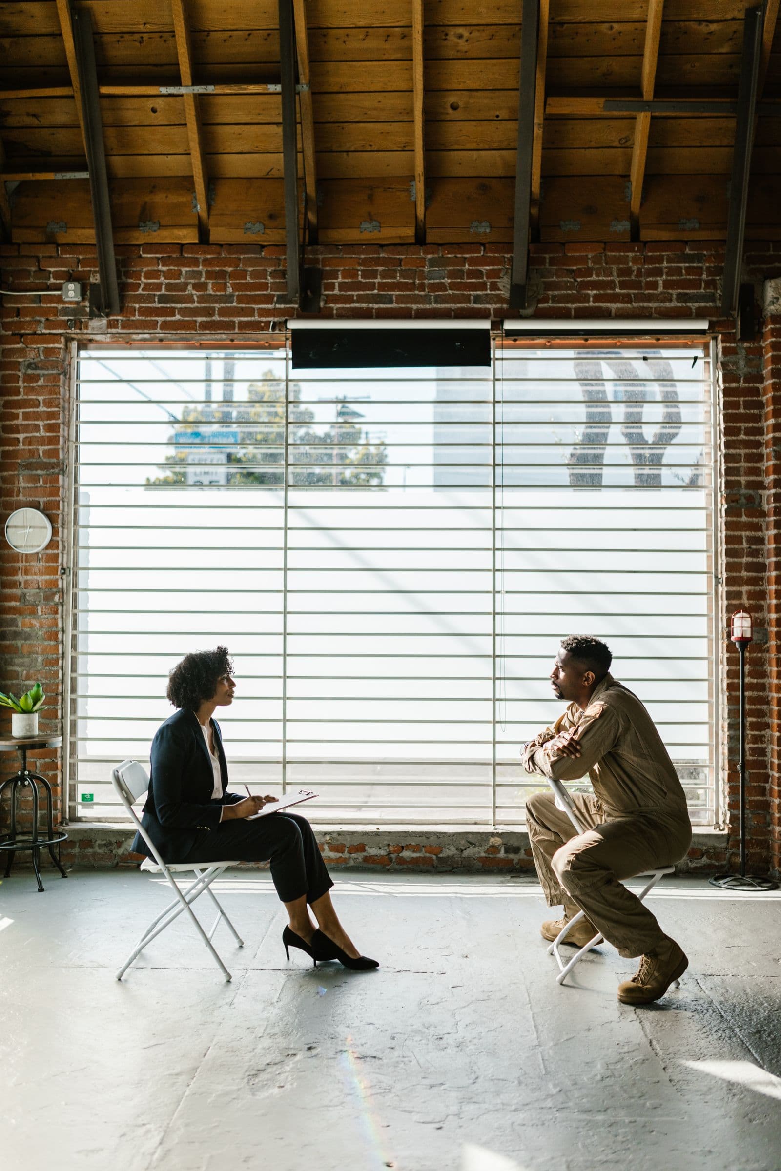 Two people sitting across from one another in a bright room, mid-conversation.